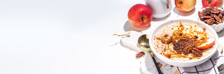 Simple autumn traditional American breakfast. Ready to eat apple pie oatmeal porridge with apples, pecans and caramel on white table background copy space