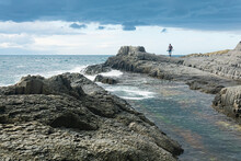 Coastal Seascape With Beautiful Columnar Basalt Rocks At Low Tide, Fisherman Is Seen In The Distance In Blur