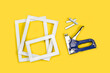 Grapadora azul y plateada de metal, grapas y marcos de madera blancos sobre un fondo amarillo brillante y aislado. Vista superior y de cerca. Copy space