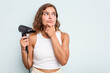 © Asier - Young caucasian woman holding a hairdryer isolated on blue background looking sideways with doubtful and skeptical expression.