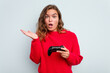 © Asier - Young caucasian gamer woman holding a game controller isolated on blue background surprised and shocked.