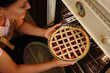 Close-up. View from above of a beautiful young woman putting baking dish with a cherry pie into oven at home kitchen. Food baking and culinary concept.