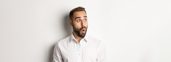 Wall Mural - Close-up of happy and surprised man looking left with amazed face, white background