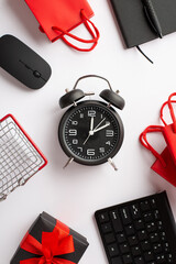 Wall Mural - Cyber monday concept. Top view vertical photo of alarm clock shopping cart keyboard computer mouse notepad pen paper bags and giftbox with red ribbon bow on isolated white background