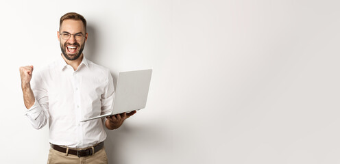 Wall Mural - Business. Happy manager winning online, rejoicing with fist pump, holding laptop and triumphing, standing over white background