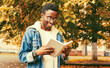 © guas - Portrait of happy smiling young african man student reading a book wearing eyeglasses in autumn city park