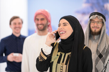 Wall Mural - Group portrait of young Muslim people women in fashionable hijab dress with three Arabian men using smartphones at modern bright home