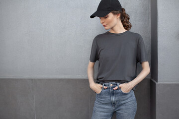 A beautiful girl is wearing a grey t-shirt, cloth cap and jeans posing against the background of a wall. fashion outfit for the city, minimalism urban style clothing