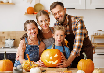 Wall Mural - Happy family mother, father and kids smiling  at camera make jack-o-lantern from pumpkin, getting ready for halloween