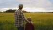 © Acronym - Farmer and his son in front of a sunset agricultural landscape. Man and a boy in a countryside field. Fatherhood, country life, farming and country lifestyle.