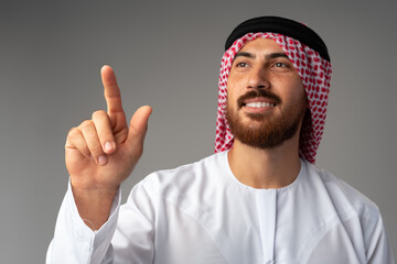 Wall Mural - Young Arab man pointing hand to copy space on gray background