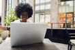 © fotofabrika - Smiling young african woman sitting with laptop in coffee shop