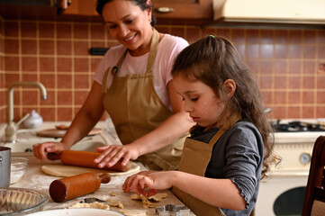 Wall Mural - Caucasian beautiful little girl and her mom in beige aprons, playing and laughing while kneading the dough in kitchen. Homemade pastry for bread, pizza or bake cookies. Family fun and cooking concept