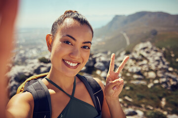 Hiking selfie, happy woman and fitness in nature on a mountain for exercise, travel and trekking adventure during summer. Face, smile and peace sign female tourist exploring outdoors with a backpack