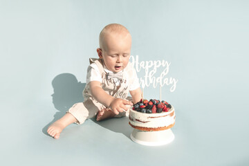 Toddler boy and first healthy homemade birthday cake with berries on blue background. Copy space. Happy, surprised one year baby boy. Child's emotions. Party celebration, greeting card