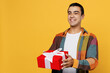 © ViDi Studio - Young smiling happy fun cool middle eastern man 20s he wear casual shirt white t-shirt holding giving red present box with gift ribbon bow isolated on plain yellow background People lifestyle concept.
