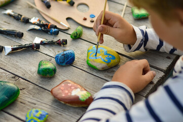 A detailed picture of a child's hands drawing a fungus on a stone with acrylic paints. Home hobbies are authentic. Artwork on stones.