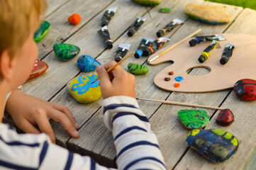 A detailed picture of a child's hands drawing a fungus on a stone with acrylic paints. Home hobbies are authentic. Artwork on stones.