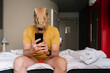 © karrastock - Man with lizard mask using the smartphone in a hotel bed.
