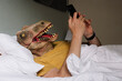 © karrastock - Man with lizard mask using the smartphone in a hotel bed.