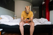 © karrastock - Man with lizard mask using the smartphone in a hotel bed.