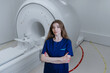 © makedonski2015 - Portrait of a young woman doctor in a blue suit who looks into the camera against the background of an MRI machine. Diagnostic laboratory in the clinic.