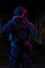 Wall Mural - Army soldier in Combat Uniforms with an assault rifle and combat helmet night mission dark background. Blue and purple gel light effect. 