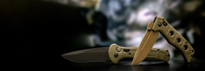 Wall Mural - Khaki military pocket folding knives. Compact metal sharp knife with a folding blade. Blurred back.