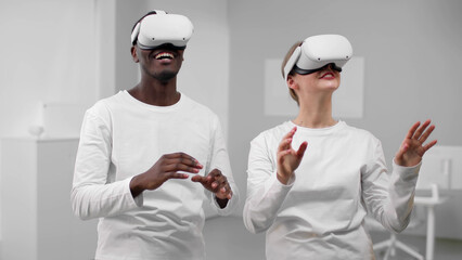 Poster - African-American man and caucasian woman in white clothes use vr goggles