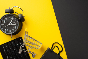 Wall Mural - Cyber monday concept. Top view photo of keyboard shopping cart alarm clock and black paper bag on bicolor yellow and black background with empty space