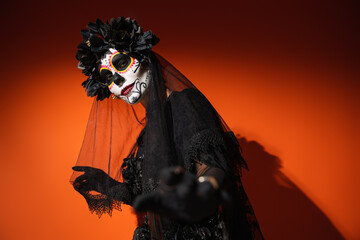 Wall Mural - Woman in santa muerte costume and creepy makeup looking at camera on red background.