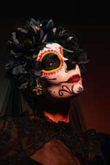 Wall Mural - Portrait of woman in mexican day of dead costume standing on burgundy background.