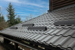 Closeup roof with metal grey shingle tiling surface with rain gutter pipe and snow guards protective fence.