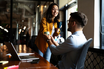 Wall Mural - Colleagues laughing in office. Businesswoman and businessman drinking coffee.