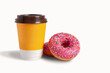Blank yellow takeaway cup of coffee with a brown lid. Glazed donut with pink icing with sprinkles nearby. Isolated on white background. Copy space, close-up