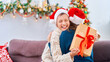 © skif - happy and loving mother and son, dressed in a Santa Claus hat, hug at home, sitting on the sofa against the background of a Christmas tree. child and woman are laughing happily while holding gift box.