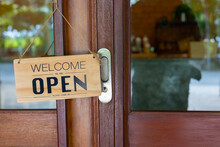 "Welcome And Open" Wording On Wooden Plate As Sign In Front Of The Entrance Or Door Of Coffee Shop, Restaurant, Bar, Pub And Grocery Store Shows Advertising Message To Customer For Business.
