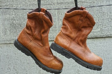 Wall Mural - a pair of leather comfortable fashionable orange boots hang on a black clothesline against a concrete wall in the street