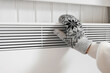 Hands in winter gloves warming up over electric heater. Frozen woman wearing a knitted mittens freezing for winter cold. Discomfort spending time at home. Girl warming hands on modern radiator.
