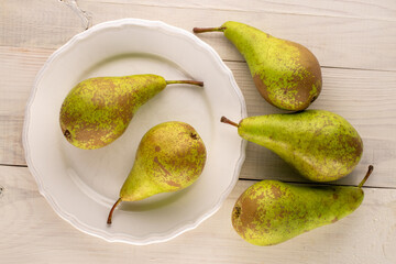 Several sweet pears with white ceramic plate on wooden table, macro, top view.