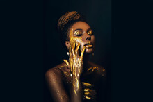 Artwork Portrait Closeup Fantasy African Woman Face In Gold Paint. Golden Shiny Skin. Fashion Model Girl Goddess. Hand Fingers In Metallic Liquid Drop. Arab Royal Style Professional Glamorous Makeup