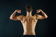 © Ursula Page - A man making muscles with his arms from behind showing a muscular and fit back on a black background