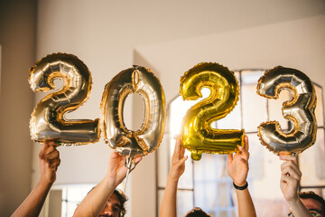 Group of friends at a party celebrate happy new 2023 year with elegant inflatable gold text - People have fun together at home