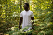 © kanashkin - African american man in a white t-shirt walks in a green forest. Mock-up