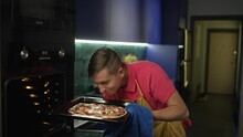 A man takes a pizza out of the oven. A boy prepares dinner for his family in the kitchen. Cooking pizza at home. High quality 4k footage