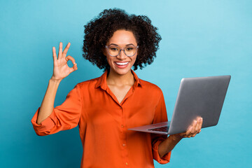 Portrait of beautiful trendy cheery wavy-haired girl using laptop showing ok-sign ad isolated on bright blue color background