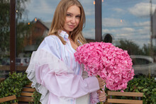 Beautiful Blond Woman In Patchwork Shirt With Bouquet Of Pink Flowers
