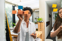 Multiracial Businesswomen Putting Post-it Notes On Glass Board