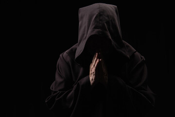 Sticker - medieval monk with face under dark hood praying isolated on black.