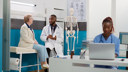 African american doctor doing consultation with senior woman in medical office, having checkup appointment. Medic consulting patient with disease at healthcare examination visit.